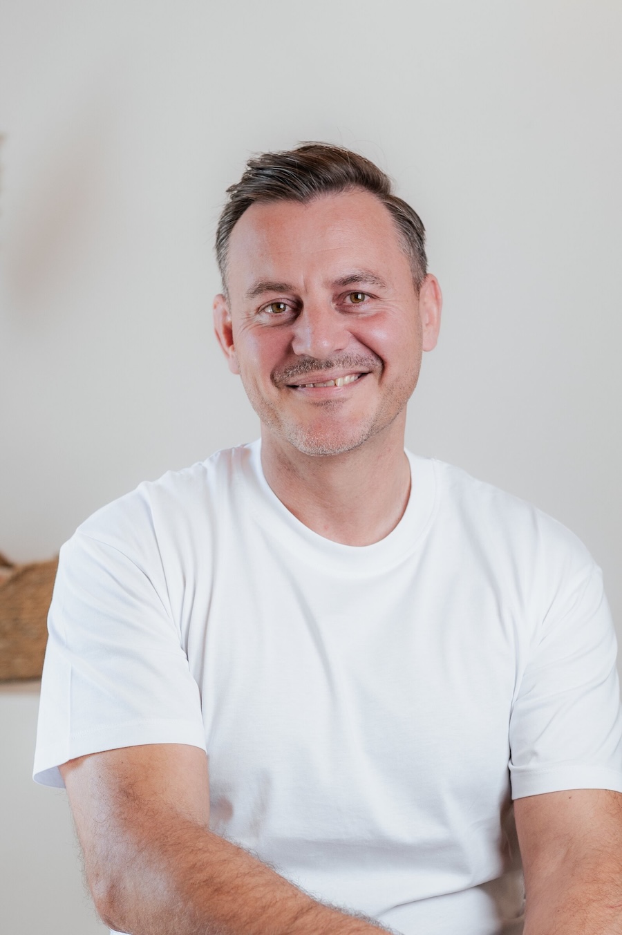 Porträt von Michael Brezina mit dunklem Haar und weißem T-Shirt, freundlich lächelnd.