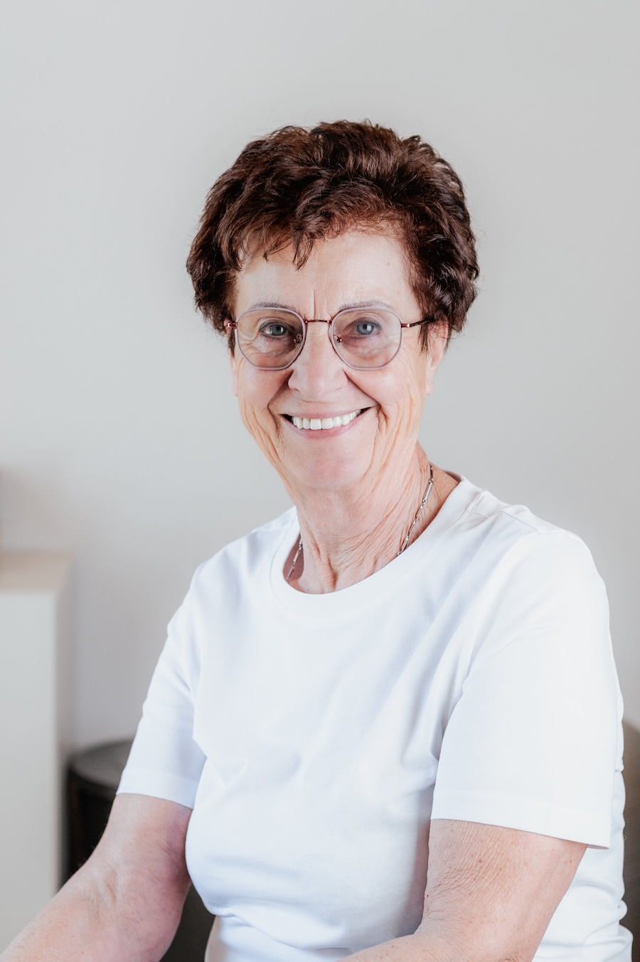 Porträt von Sonja Brezina mit Brille, kurzem dunklem Haar und weißem T-Shirt, lächelnd.